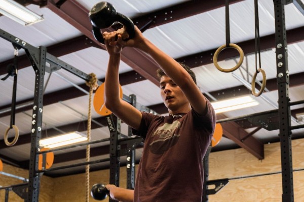 young man lifting a kettle bell in kids crossfit class